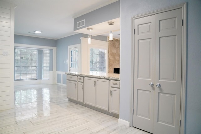 kitchen with crown molding, white cabinetry, light stone counters, decorative light fixtures, and light wood-type flooring