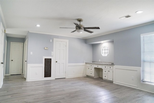 unfurnished office with crown molding, light hardwood / wood-style flooring, ceiling fan, built in desk, and a textured ceiling