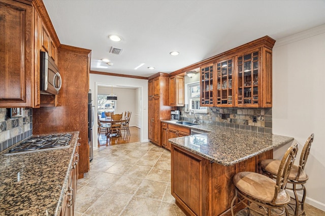 kitchen with a kitchen bar, sink, dark stone counters, kitchen peninsula, and stainless steel appliances