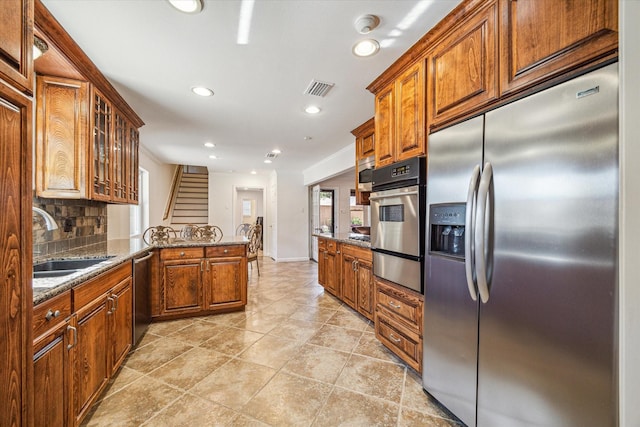 kitchen featuring sink, dark stone countertops, stainless steel appliances, tasteful backsplash, and kitchen peninsula