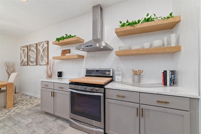 kitchen with stainless steel stove, gray cabinetry, light stone counters, decorative backsplash, and wall chimney exhaust hood