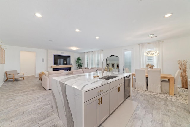 kitchen with sink, light hardwood / wood-style flooring, dishwasher, light stone countertops, and an island with sink