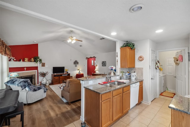 kitchen featuring sink, white dishwasher, a fireplace, washer and dryer, and stone countertops