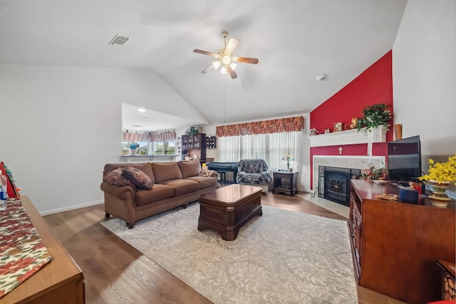 living room featuring lofted ceiling, hardwood / wood-style floors, a tiled fireplace, and ceiling fan