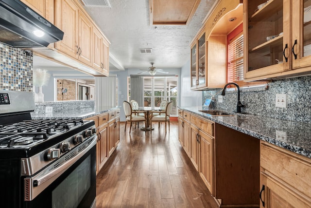 kitchen with sink, dark stone countertops, dark hardwood / wood-style floors, stainless steel range with gas stovetop, and ceiling fan