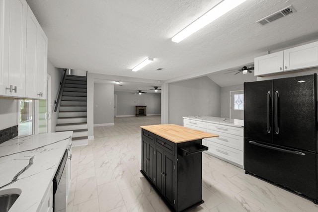 kitchen featuring white cabinetry, butcher block counters, a center island, black fridge, and a textured ceiling