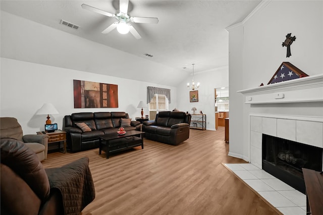 living room with ceiling fan with notable chandelier, light hardwood / wood-style floors, vaulted ceiling, and a tile fireplace