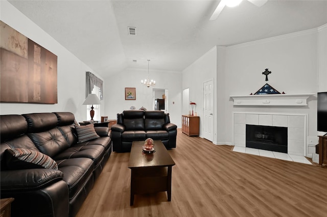 living room with a tiled fireplace, vaulted ceiling, crown molding, and light hardwood / wood-style flooring