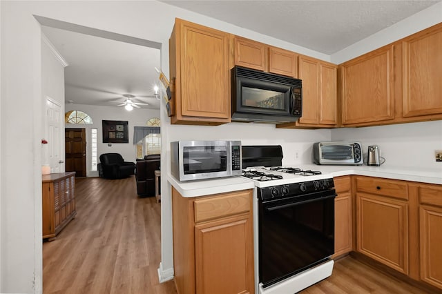 kitchen with ceiling fan, gas range oven, and light wood-type flooring