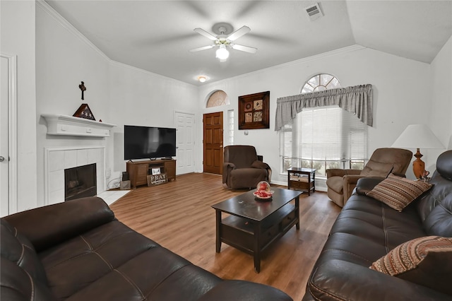 living room with wood-type flooring, vaulted ceiling, ornamental molding, ceiling fan, and a fireplace