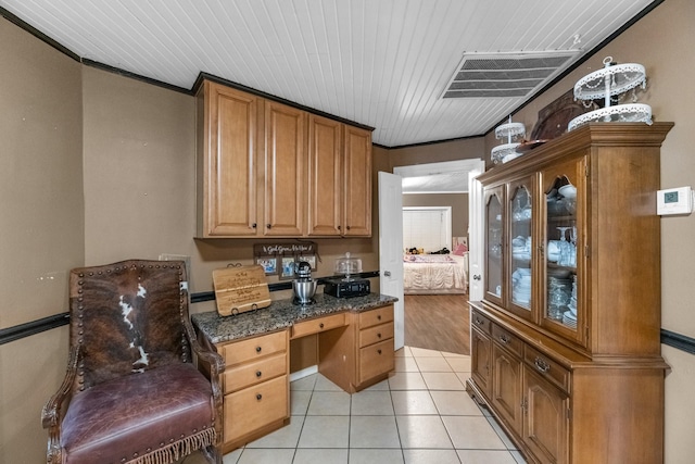 kitchen featuring light tile patterned floors, visible vents, glass insert cabinets, ornamental molding, and dark stone countertops