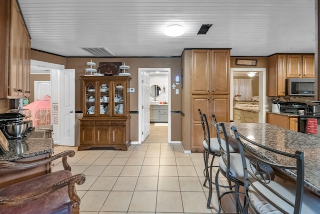 kitchen featuring light tile patterned floors, visible vents, stainless steel microwave, brown cabinets, and black / electric stove