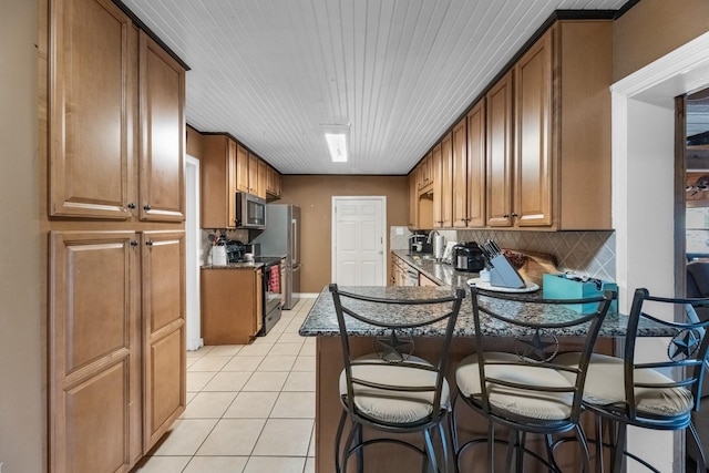 kitchen with light tile patterned floors, stainless steel appliances, brown cabinetry, and a kitchen breakfast bar