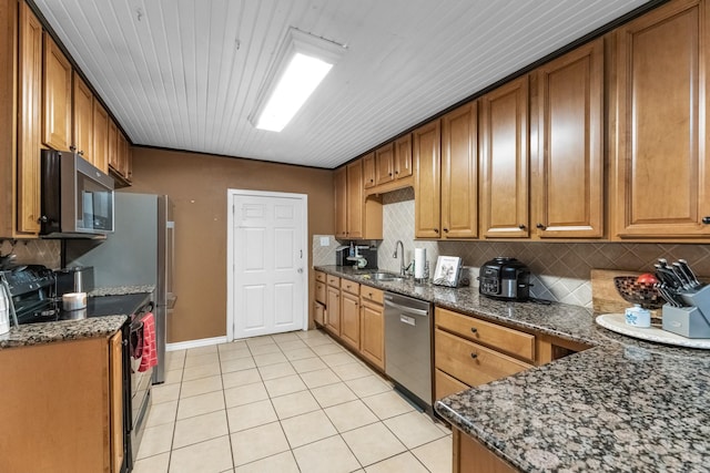 kitchen with light tile patterned floors, a sink, appliances with stainless steel finishes, decorative backsplash, and brown cabinets