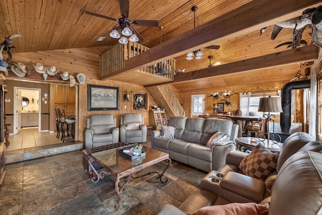 living area with stairway, a ceiling fan, a wood stove, wood walls, and wooden ceiling