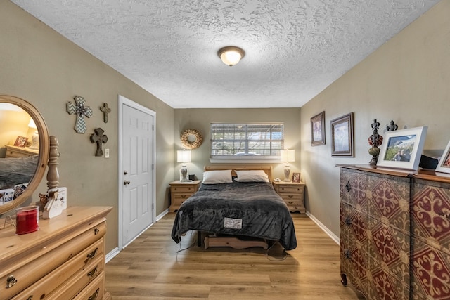 bedroom featuring light wood-style floors, baseboards, and a textured ceiling