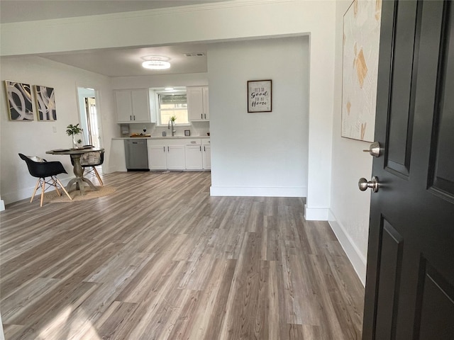 kitchen with light countertops, white cabinets, a sink, wood finished floors, and baseboards