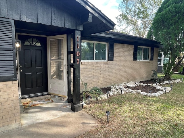 property entrance with brick siding and a lawn