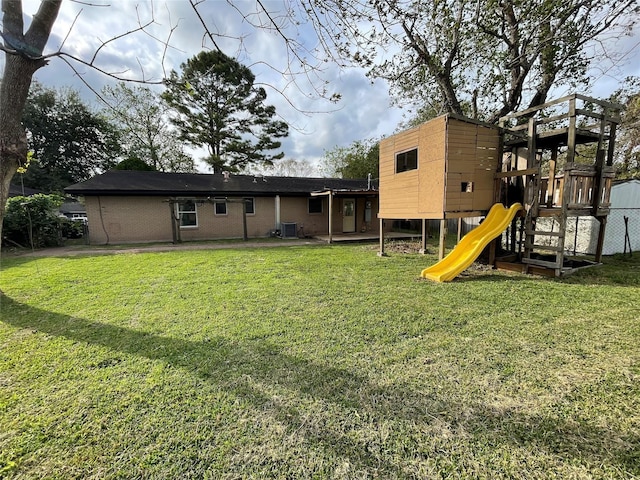 back of house featuring a playground, a yard, brick siding, and central AC unit