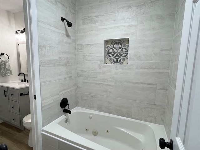 bathroom featuring a combined bath / shower with jetted tub, toilet, wood finished floors, and vanity