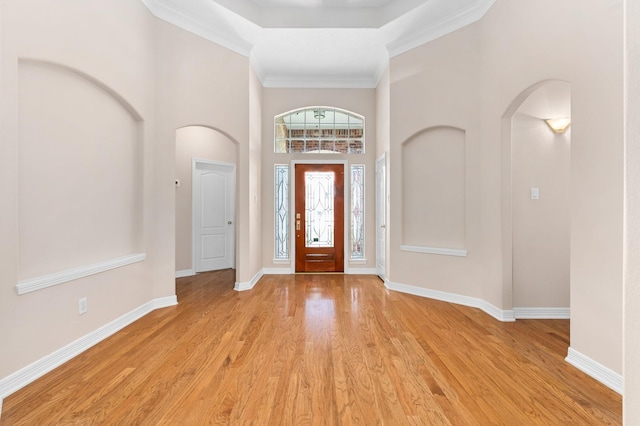 foyer entrance with ornamental molding, a towering ceiling, and light wood-type flooring