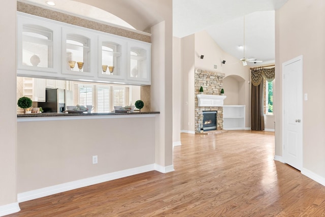 interior space with light hardwood / wood-style flooring, ceiling fan, white cabinets, stainless steel fridge with ice dispenser, and a stone fireplace