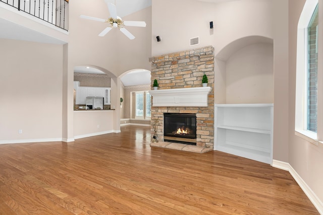 unfurnished living room featuring a high ceiling, a stone fireplace, ceiling fan, and light wood-type flooring