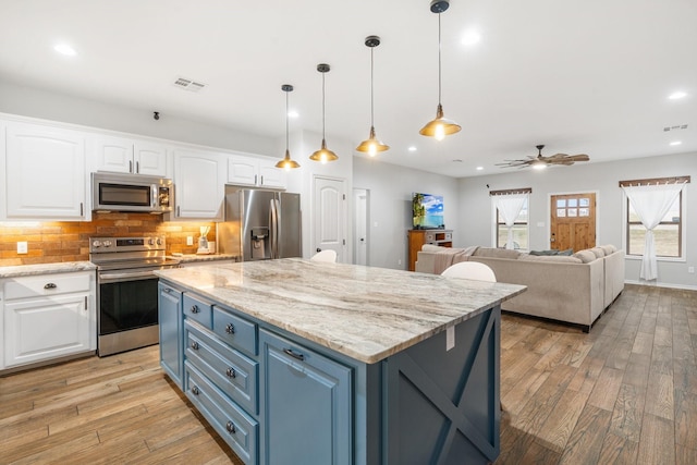 kitchen featuring blue cabinets, a center island, appliances with stainless steel finishes, pendant lighting, and white cabinets