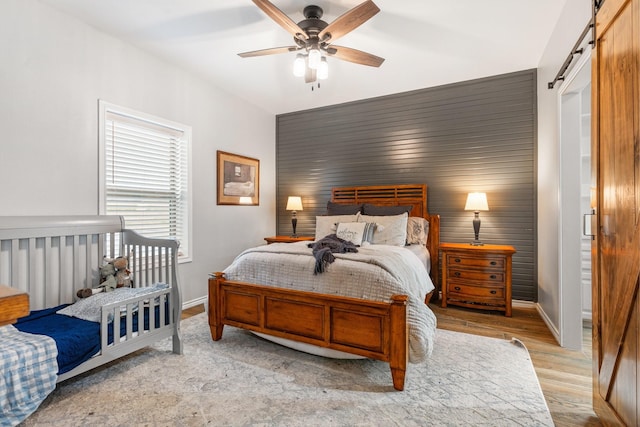 bedroom with light hardwood / wood-style floors, a barn door, ceiling fan, and wood walls