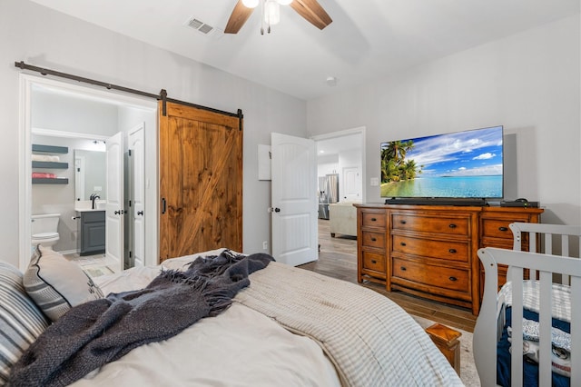 bedroom with ensuite bathroom, hardwood / wood-style floors, sink, ceiling fan, and a barn door