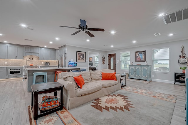 living room with crown molding, ceiling fan, sink, and light wood-type flooring