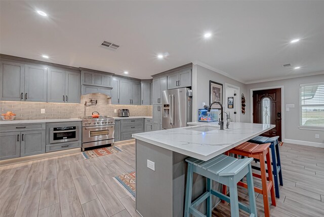 kitchen featuring a breakfast bar, high quality appliances, sink, a kitchen island with sink, and light stone counters