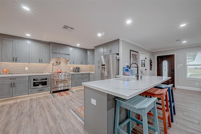 kitchen with sink, a breakfast bar area, high end appliances, light stone counters, and a center island with sink