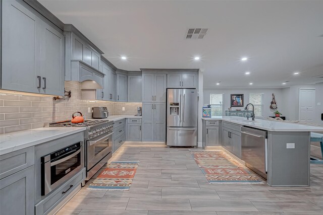 kitchen featuring sink, gray cabinetry, a breakfast bar area, backsplash, and stainless steel appliances