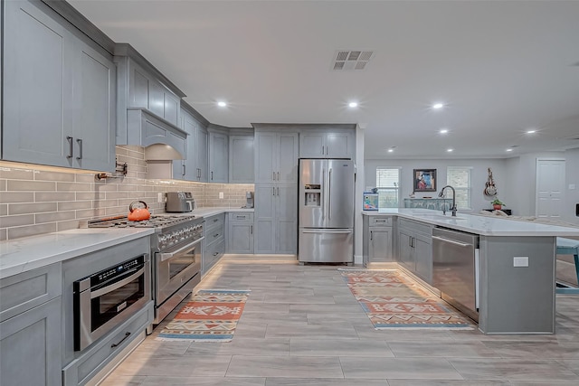 kitchen featuring sink, a breakfast bar area, gray cabinets, stainless steel appliances, and decorative backsplash