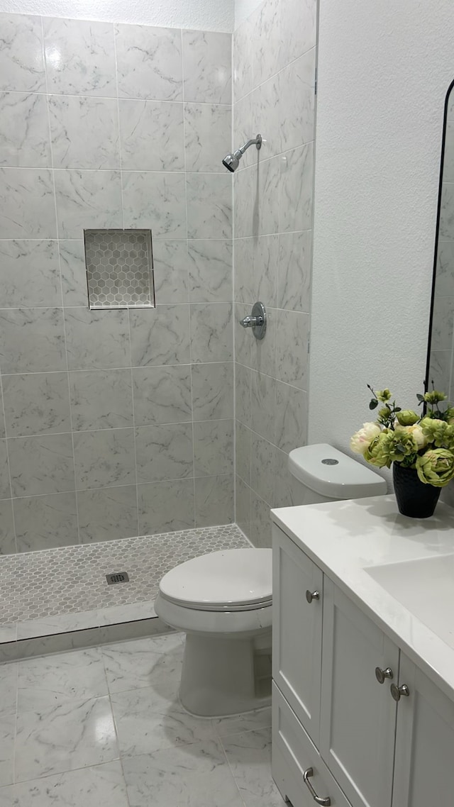 bathroom featuring tiled shower, vanity, and toilet