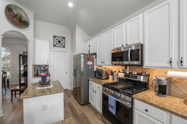 kitchen with stainless steel appliances, light stone countertops, a center island, and white cabinets