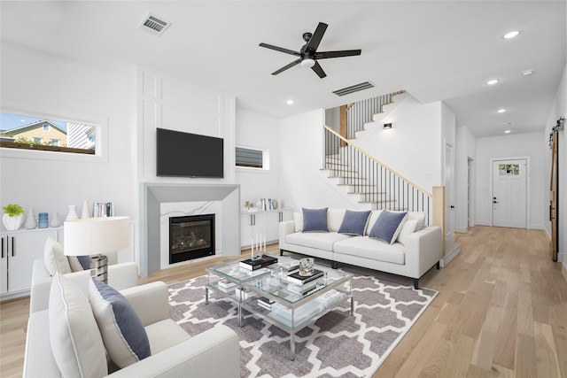 living room featuring a premium fireplace, ceiling fan, and light hardwood / wood-style flooring