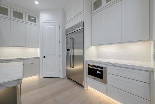 kitchen featuring white cabinetry, light stone counters, light hardwood / wood-style flooring, and stainless steel appliances