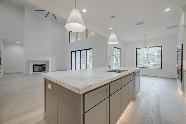 kitchen featuring gray cabinetry, sink, decorative light fixtures, and a center island with sink