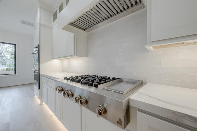 kitchen featuring backsplash, light stone countertops, custom exhaust hood, and white cabinets