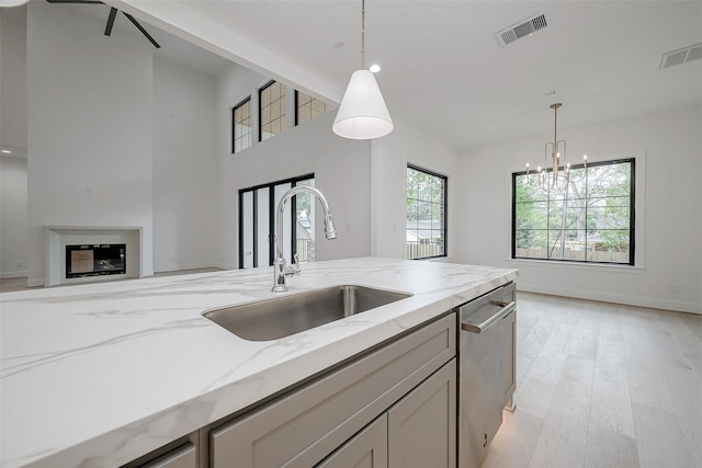 kitchen with light stone counters, dishwasher, sink, and hanging light fixtures