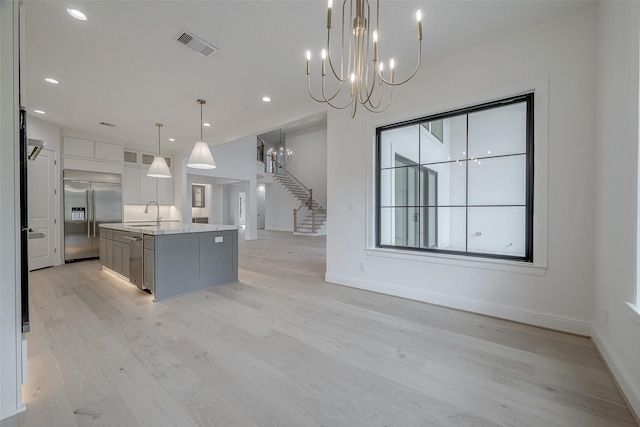 kitchen with an inviting chandelier, decorative light fixtures, a large island with sink, stainless steel appliances, and light stone countertops