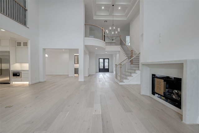 unfurnished living room featuring a towering ceiling, light wood-type flooring, a chandelier, coffered ceiling, and beam ceiling