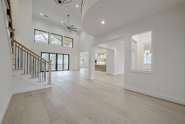 unfurnished living room featuring ceiling fan, a towering ceiling, and light wood-type flooring