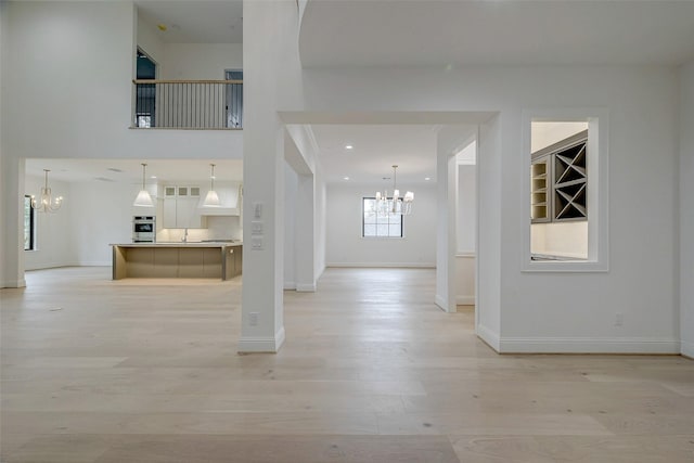 foyer entrance featuring sink, a towering ceiling, a chandelier, and light wood-type flooring