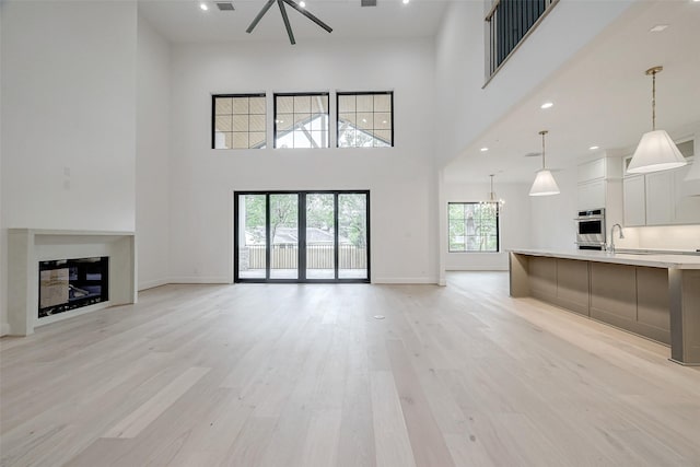 unfurnished living room with a high ceiling, sink, a notable chandelier, and light hardwood / wood-style flooring