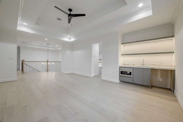 interior space with ceiling fan with notable chandelier, sink, ornamental molding, light hardwood / wood-style floors, and a tray ceiling