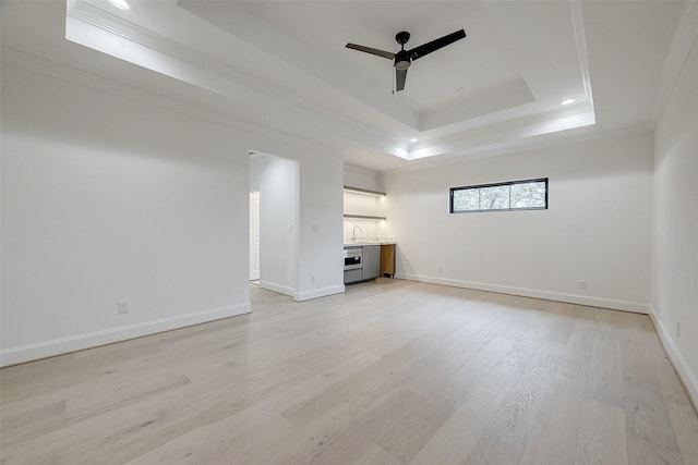 unfurnished living room featuring sink, ornamental molding, a raised ceiling, ceiling fan, and light hardwood / wood-style floors