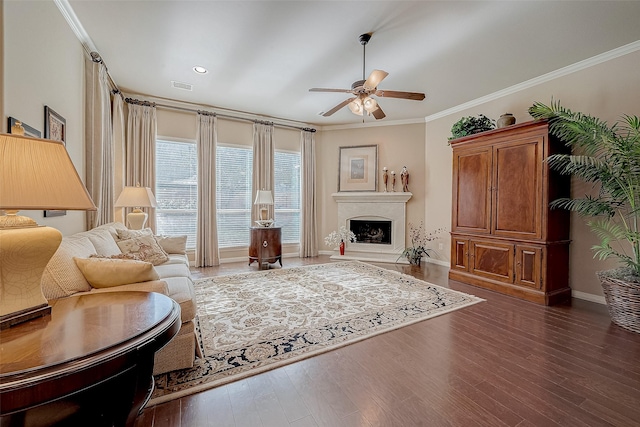 living room with dark wood-type flooring, a high end fireplace, ornamental molding, and ceiling fan